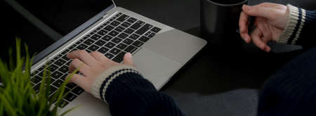 Cropped shot of businesswoman relaxing with hot coffee while working with laptop at dark modern...