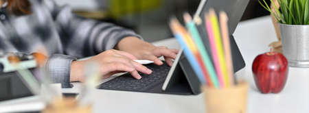 Side view of female graphic designer typing on digital tablet on worktable with camera, stationery...