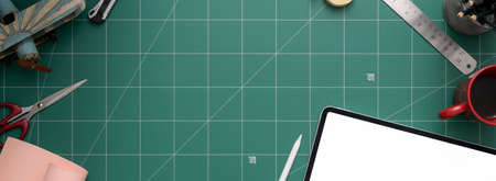 Overhead shot of workspace with mock-up tablet, scissor, supplies and copy space on cutting mat