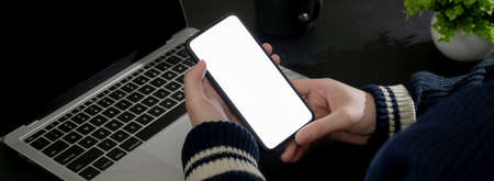 Cropped shot of businesswoman relaxing with mock-up smartphone while sitting at dark modern worktableの写真素材