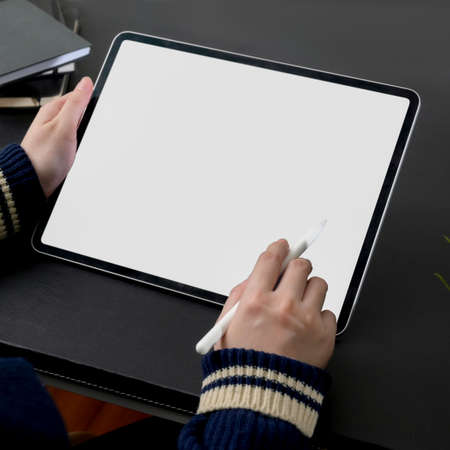 Cropped shot of female freelancer working on blank screen tablet with stylus at dark modern...