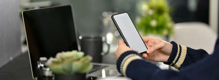 Side view of female freelancer looking on mock-up smartphone while sitting at dark modern workplace