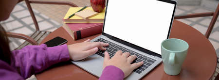 Cropped shot of female university student doing her assignment with blank screen laptop and books on...