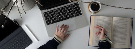 Overhead shot of female university student preparing for her upcoming exam with book and digital devices on white worktableの写真素材