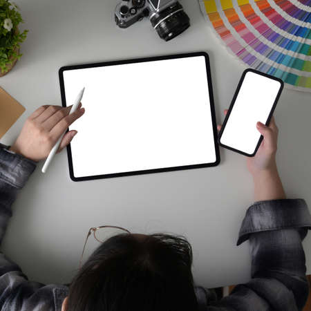 Overhead shot of female freelancer working on her project with mock-up tablet, smartphone and designer supplies on white tableの写真素材