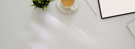 Overhead shot of minimal designer worktable with mock-up tablet, supplies, tea cup and copy space on white worktableの写真素材