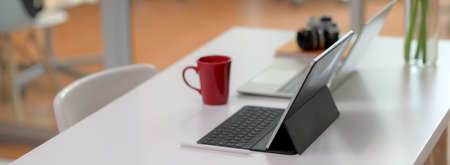 Comfortable office desk with laptop, digital tablet, mug, camera, office supplies and decoration on white table with chairの写真素材