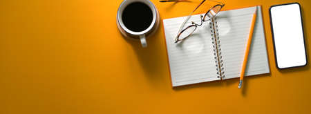 Top view of creative worktable with blank screen smartphone, diary notebook, coffee cup, eyeglasses...