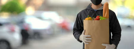 Close up view of food delivery service man holding fresh food bag while waiting for his customer