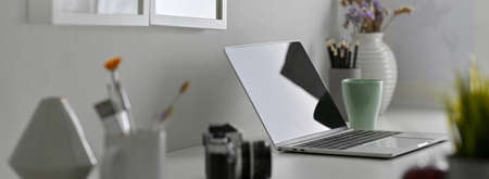 Side view of designer office desk with laptop, painting tools, camera and decorations on white tableの写真素材