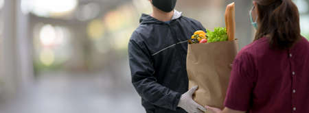 Panoramic banner of food delivery service man delivered fresh food bag to young female customer at her home の写真素材