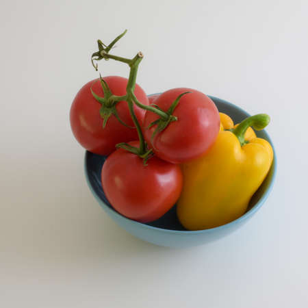 close up view of vegetables bowl with tomatoes and bell pepper on white kitchen deskの写真素材