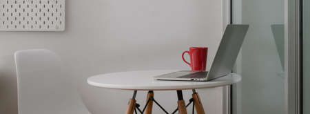 Side view of portable workspace with laptop, coffee mug and copy space on white circle tableの写真素材