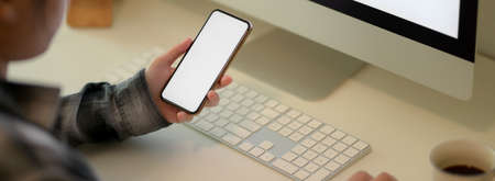 Cropped shot of businesswoman looking information on mock-up smartphone on white office desk with...