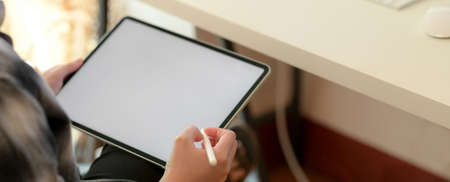 Cropped shot of businesswoman working on blank screen tablet on white office desk with computer...