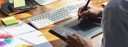 Close up view of graphic designer working with drawing tablet and computer device on wooden...
