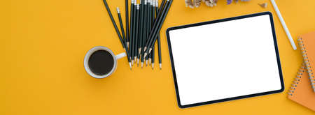 Top view of creative worktable with blank screen tablet, pencils and coffee cup on yellow desk  
