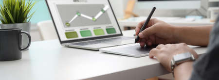 Cropped shot of graphic designer working on infographic project with drawing tablet and laptop on white office deskの写真素材