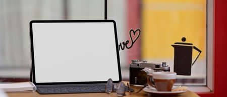 Close up view of portable workspace with mock-up tablet, camera, glasses and coffee cup on wooden counter bar in cafeの写真素材