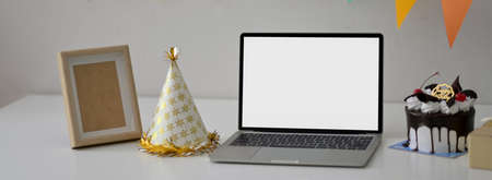 Online party concept with blank screen laptop, party hat and mock-up frame on white deskの写真素材