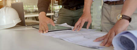 Cropped shot of two engineers working together with mock-up tablet and paperwork on white table in meeting room の写真素材