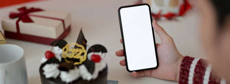 Online Birthday celebration concept, female holding blank screen smartphone on white table with cake...