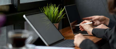 Side view of two businesspeople working together on wooden bar in cafe with digital device, coffee...