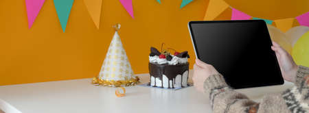 Cropped shot of female holding digital tablet while sitting at table with cake and party hatの写真素材