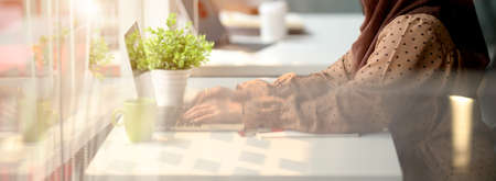 View through window of female entrepreneur working with laptop, coffee mug and decoration on white...