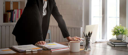 Cropped shot of female entrepreneur standing at her office desk and looking informations on laptopの写真素材