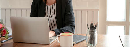 Close up view of female entrepreneur working with laptop, stationery and coffee mug on wooden office...