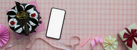 Overhead shot of pink scott pattern background with mock-up smartphone, Black Forest cake, decorations and copy space の写真素材