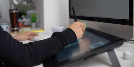 Side view of female graphic designer working on drawing tablet and computer on office desk 