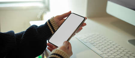 Close up view of female freelancer using mock-up smartphone while sitting at worktable