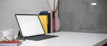 Side view of stylish worktable with mock-up tablet, glasses, books, vase and copy space on white...