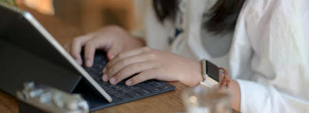 Close up view of female freelancer typing on tablet keyboard while sitting at portable workspaceの写真素材