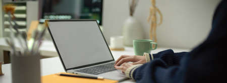 Cropped shot of female employee working on mock-up laptop with mug and stationery on portable workspace in office roomの写真素材