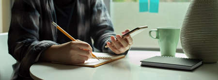 Side view of female freelancer sitting decide window and noting on schedule book while looking...