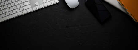 Top view of dark modern workspace with computer device, smartphone, notebooks and copy space on black tableの写真素材