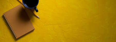 Top view of creative workspace with stationery, coffee cup and copy space on yellow concrete backgroundの写真素材