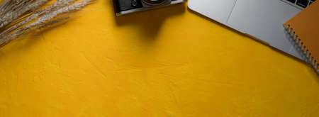 Top view of creative workspace with laptop, camera, schedule book and copy space on yellow concrete backgroundの写真素材
