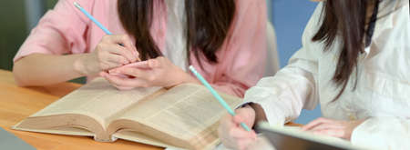 Close up view of female college students doing an assignment together with book and stationeryの写真素材