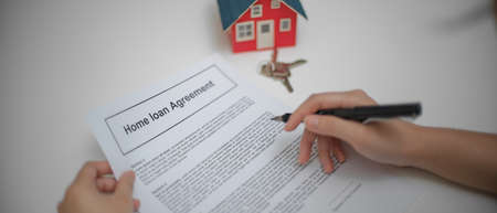Close up view of a woman reading home loan agreement to consider before sign contract on table with house modelの写真素材