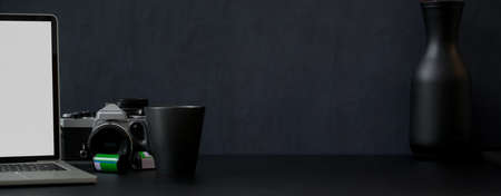 Close up view of dark modern office desk  with mock-up laptop, camera, mug, decoration and copy space の写真素材