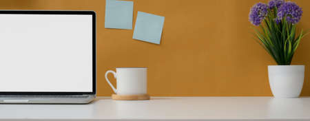 Close up view of comfortable workspace with mock-up laptop, cup, flower pot and copy space on white...
