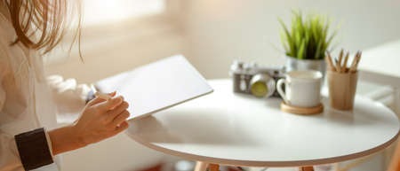 Close up view of female freelancer using digital tablet while sitting  at coffee table beside window...