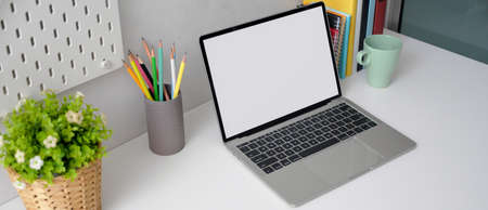 Cropped shot of home office desk with mock-up laptop, stationery, books and tree pot on white tableの写真素材