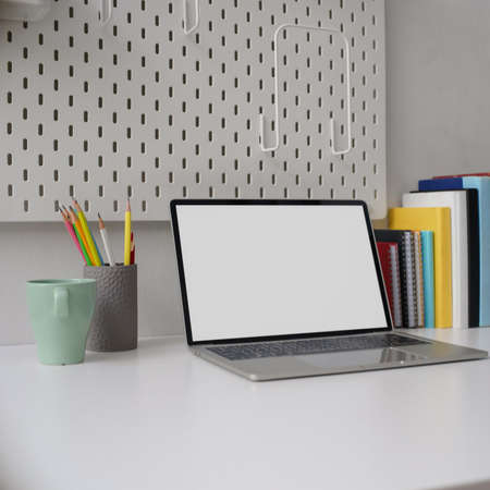 Cropped shot of stylish home office with blank screen laptop, mug, stationery and books on white...