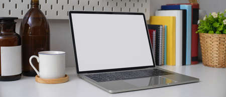 Cropped shot of stylish home office desk with mock-up laptop, books, cup and decorations on white...