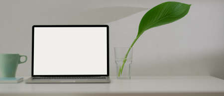 Close up view of minimal worktable with blank screen laptop, mug, schedule book and plant in a glass vaseの写真素材